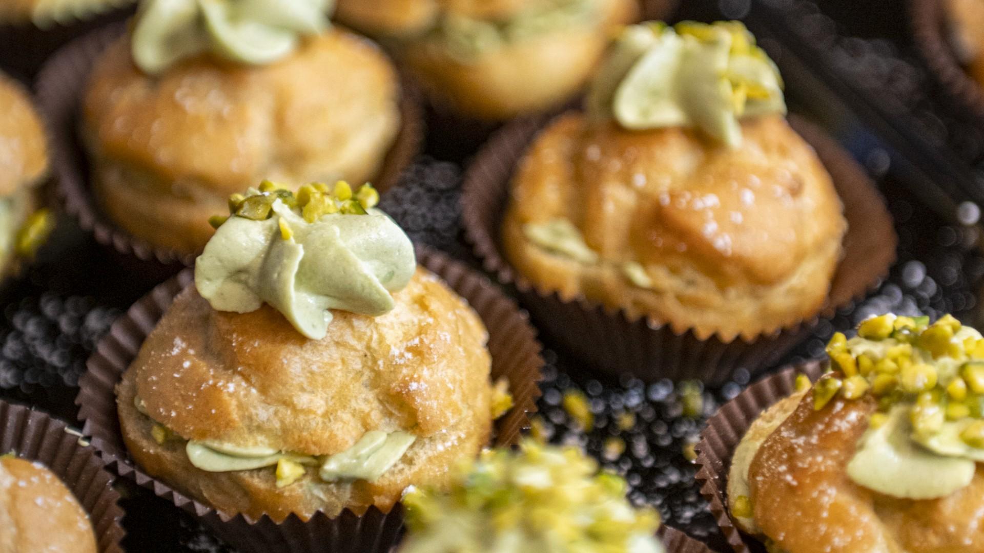 Bignè al pistacchio con crema e granella, serviti in pirottini di carta.