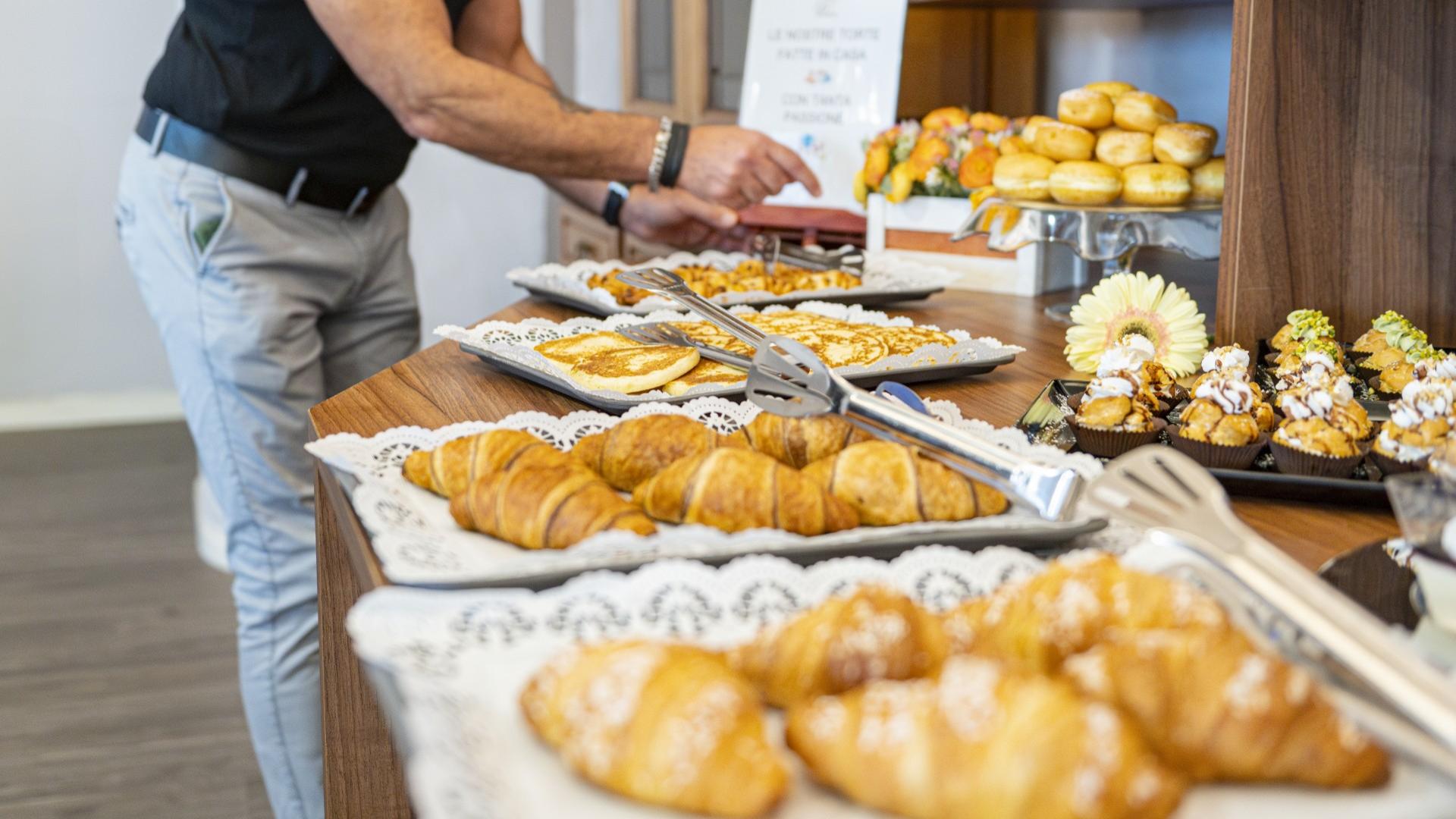 Buffet di dolci con croissant, pancake e pasticcini assortiti su vassoi eleganti.