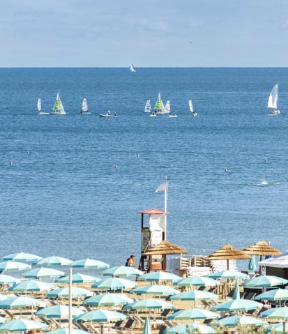 Spiaggia con ombrelloni e barche a vela sul mare azzurro.