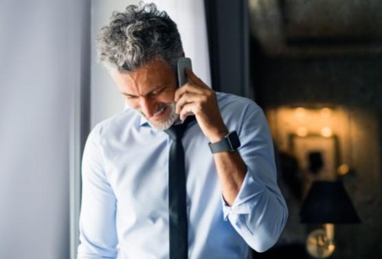 Uomo d'affari al telefono, camicia bianca e cravatta nera, orologio al polso.