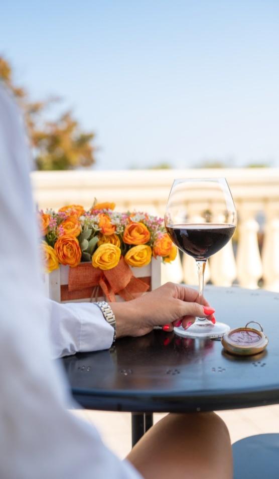 Donna con bicchiere di vino rosso, fiori arancioni, seduta a un tavolo all'aperto.