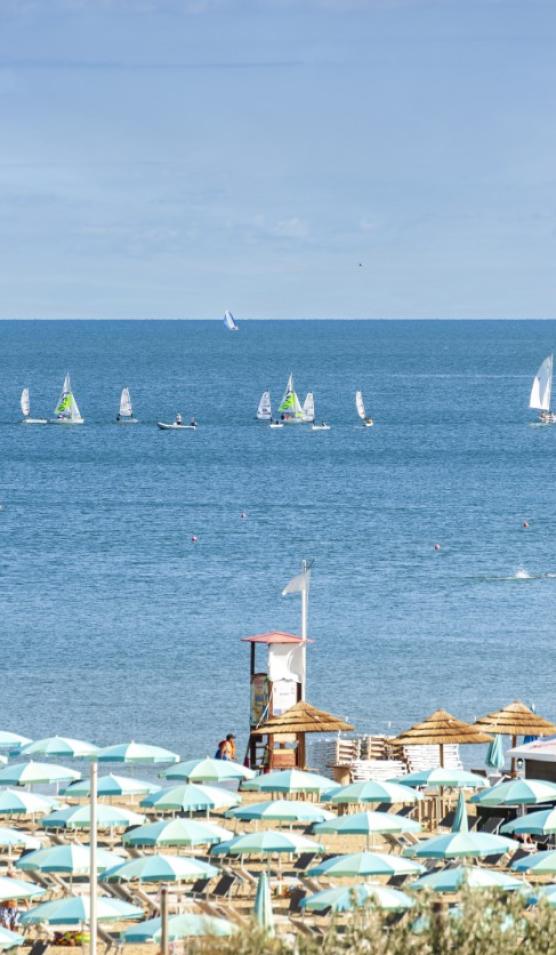 Spiaggia con ombrelloni e barche a vela sul mare.