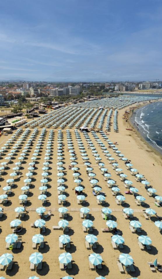 Spiaggia affollata con ombrelloni azzurri disposti in file ordinate lungo la costa.