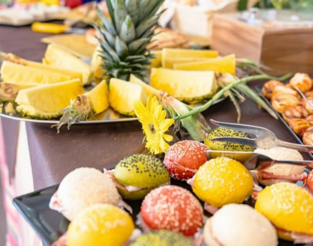 Buffet con ananas, panini colorati e fiori gialli su un tavolo elegante.