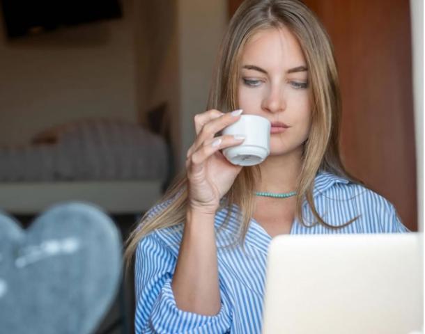 Donna beve caffè mentre lavora al computer in una stanza.