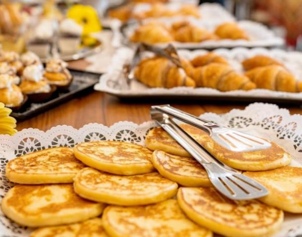 Colazione con pancake e croissant su vassoi decorati con pizzi bianchi.