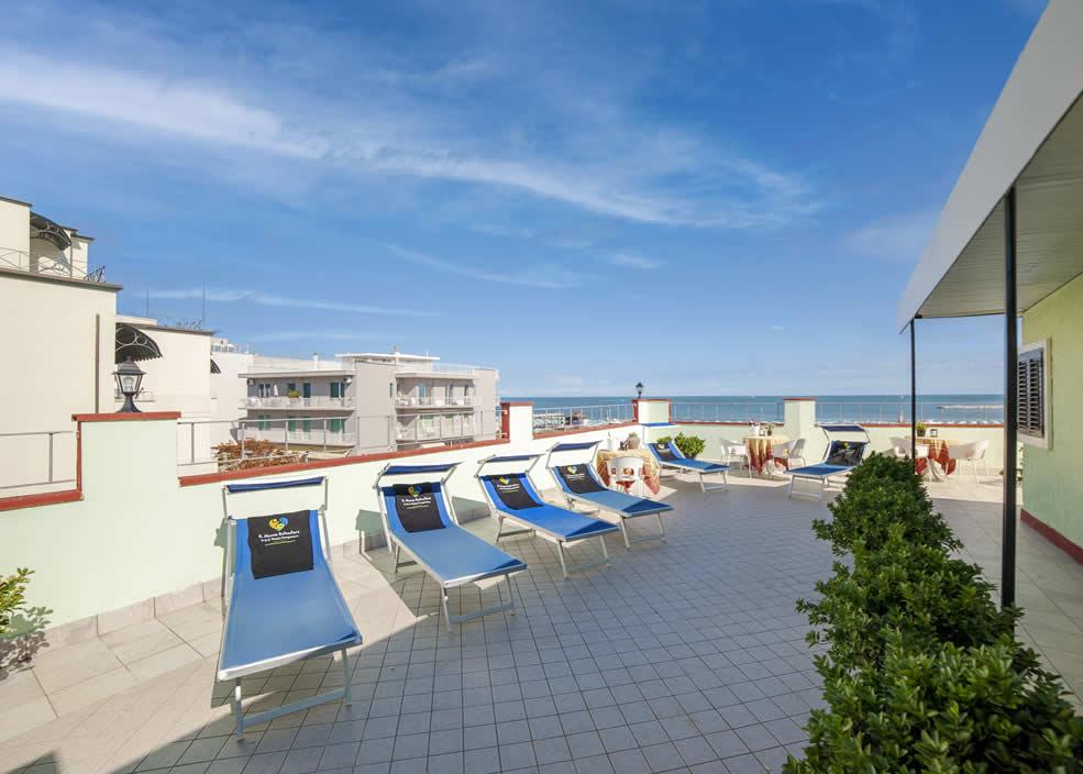 Terrazza con lettini blu, vista mare e cielo sereno.