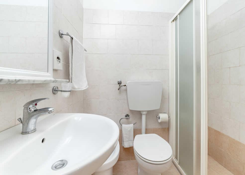 Bagno compatto con lavabo, WC e doccia, piastrelle chiare e asciugamani appesi.