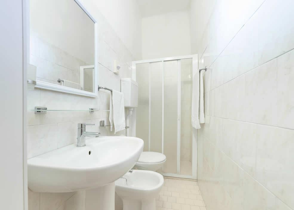 Bagno bianco con doccia, lavabo, bidet e asciugamani appesi al muro.