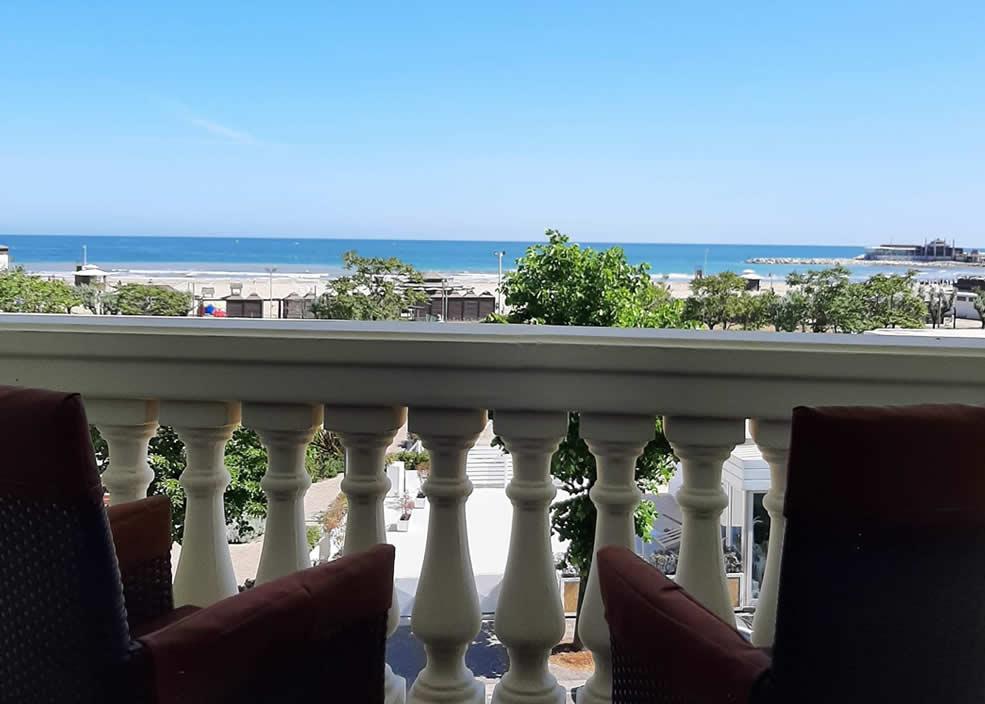 Vista sul mare da un balcone con sedie, cielo sereno e spiaggia.