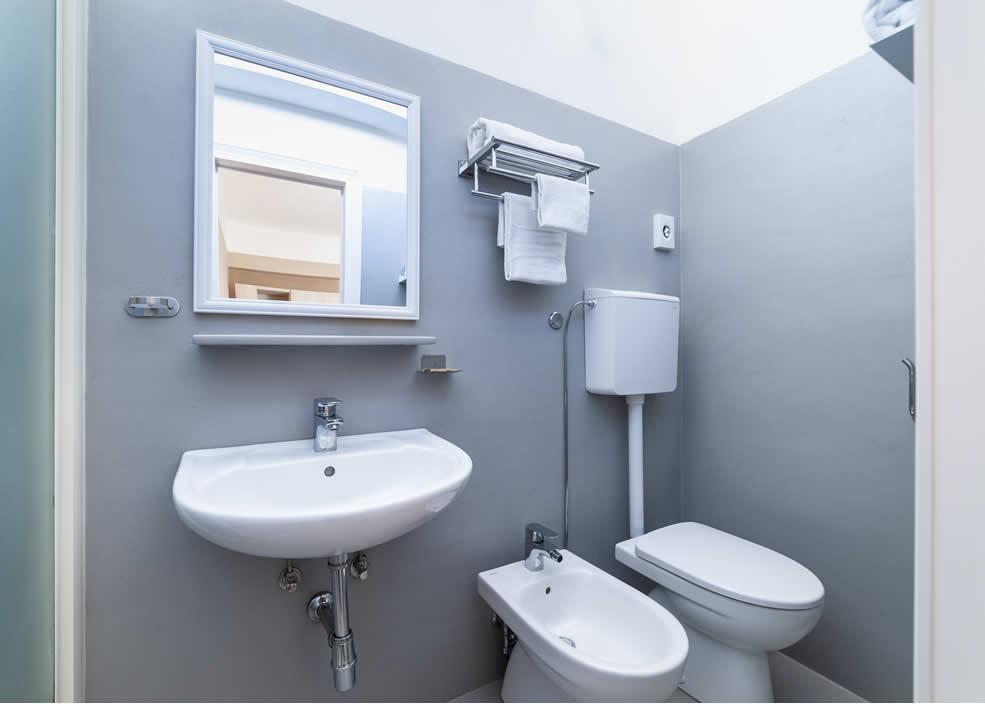 Bagno moderno con lavandino, bidet, WC e specchio, pareti grigie.