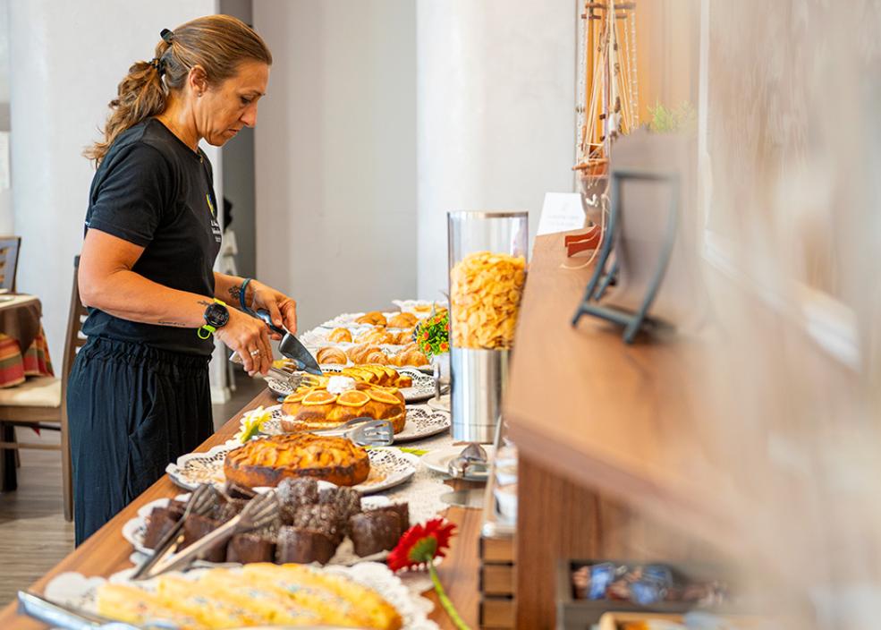 Donna prepara buffet con dolci assortiti in un ambiente luminoso e accogliente.